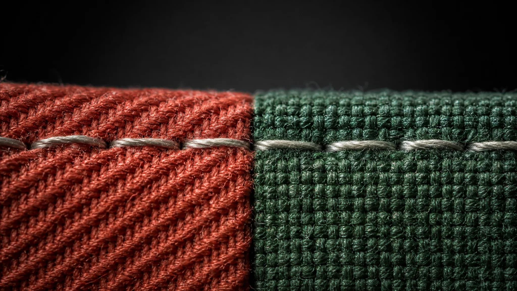 Macro of one row of stitching passing from a rust twill into a green plain weave.