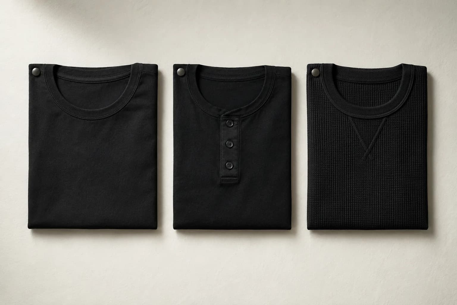 Three dark garments folded and laid out in a row on pale archival paper.