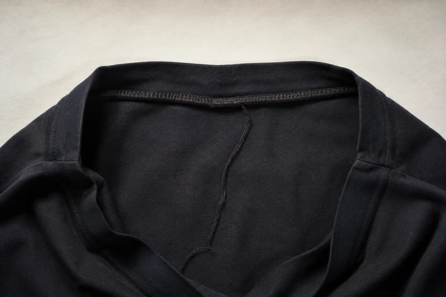 The inside neckline of a dark garment folded open, showing an overlocked seam.